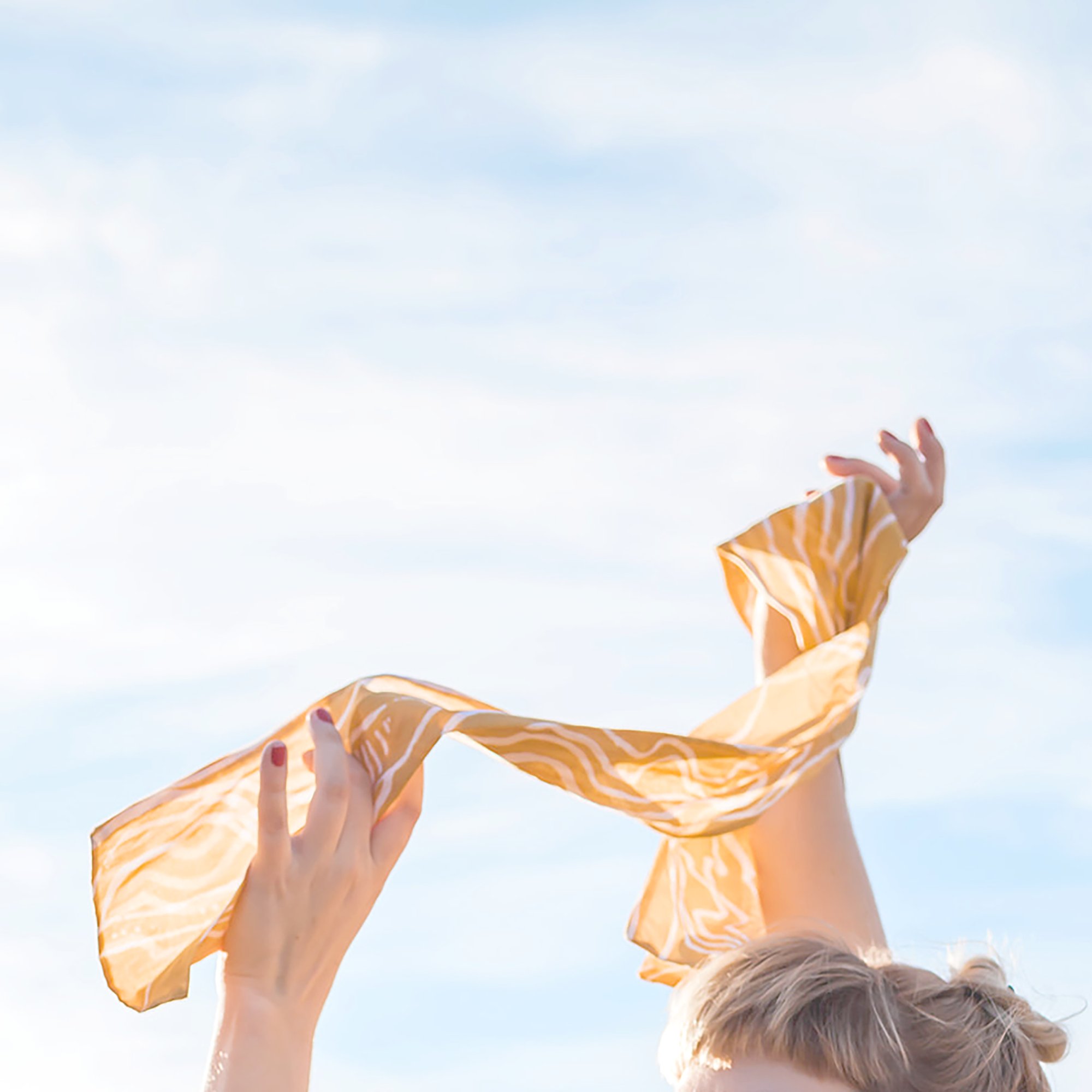 Artist holding an ochre and white printed silk wrap scarf against open landscape